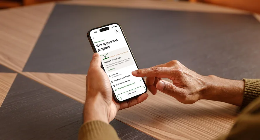 Person holding a smartphone displaying an app screen with an appeal progress update and address details.